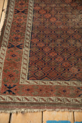 Antique Belouch rug corner showing geometric lattice, faded red, navy, and worn fringe.