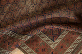 Geometric diamond lattice in dusty raspberry, navy, and brown on an antique Belouch rug.