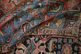 Folded vintage Heriz carpet with textured angular patterns in blush, sapphire, and dusty gold.