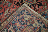 Vintage Heriz carpet corner features geometric patterns, worn pile, brown selvage, and white fringe.