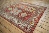 Vintage Oushak carpet with repeating floral panels in red, orange, and silver shown at an angle.