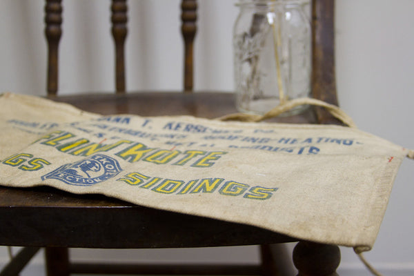 Angled detail of the vintage Flintkote apron showing its blue logo and yellow lettering.