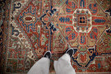 Vintage Heriz carpet displaying geometric motifs, serrated leaves, green tones, and abrashes.