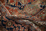 Folded vintage Heriz rug detail, revealing navy, brick red, and jade green patterns with wear.