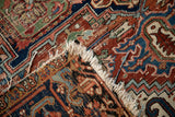 Detail of vintage Heriz carpet, showing hand-knotted navy, red, green patterns and tattered fringe.