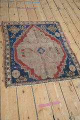 Close-up of the antique Caucasian rug's worn beige field, with primitive indigo blue and red patterns.