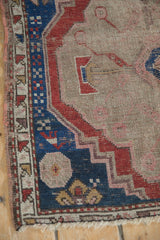 Corner of antique Caucasian rug with indigo border, primitive checkered motifs, and worn pile.