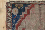Antique Caucasian rug corner, displaying foundation wear amidst geometric blue and cherry red motifs.