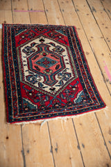 Angled view of a vintage Hamadan rug with a cherry red field and a geometric diamond medallion.