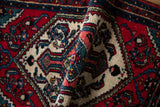 A vintage Hamadan rug curled to reveal its plush wool pile and floral motifs.