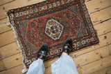 Tattered fringe and worn brick red and navy geometric pattern on a Hamadan rug.