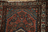 Vintage Hamadan rug corner, displaying brick red geometric blossoms and a tattered fringe.