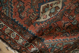 Hand-knotted pile detail, vintage Hamadan rug's brick red and dusty navy geometric motifs, worn edge.
