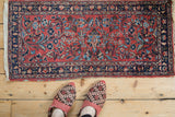 Vintage Persian Lilihan rug mat with a red field and blue border, viewed from above to show scale.