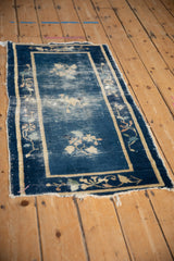 Tattered corner of antique Peking rug showing worn cobalt blue field, beige border, and floral motifs.