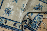 Detail of an antique Chinese Peking rug showing foundation wear, tattered fringe, blue floral motifs.