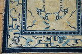 Corner of an antique Peking rug, showing cobalt blue geometric border and uneven fringe.