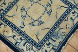 Corner of antique Peking rug, showing geometric border arabesques, floral tendrils, and tattered fringe.