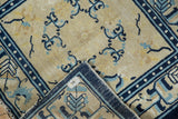 Peking antique rug corner shows hand-knotted back, cobalt powder blue geometric border, tattered fringe.