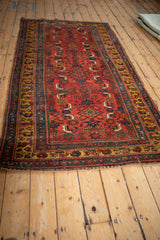 A long view of an antique Kurdish Bijar rug, emphasizing its ruby red Herati pattern and saffron borders.