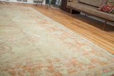 Angled view of an Oushak carpet showing sprawling ivory and softened orange designs.