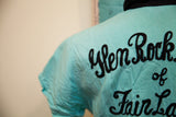 Intricate black script embroidery 'Glen Rock of Fair La' on turquoise bowling shirt back.