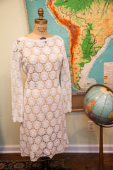 White crocheted lace dress close-up, showing intricate daisy pattern and scalloped hem.