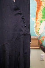 Navy blue 1920s day dress with angled placket, five black buttons, and pleats.
