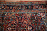 Saturated navy blue and brick red floral motifs on the hand-knotted border of a Persian Heriz rug.