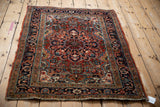 Angled view of a vintage Heriz rug with a brick red field and a scalloped navy blue medallion.