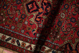 Folded vintage Hamadan rug detail: ruby red field, intricate Herati motif, and pale floral border.