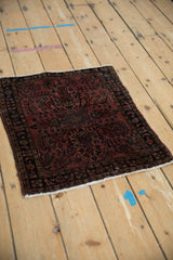 Angled view of a vintage German Sarouk mat with a floral medallion in raspberry and navy.