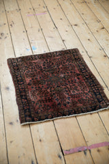 Angled view of a vintage Sarouk rug mat with a raspberry floral medallion and dark charcoal borders.