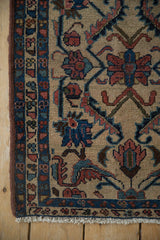 Corner of antique Persian Lilihan rug, ivory field with interlaced vines, blue border, visible fringe.