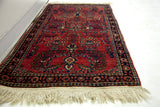 Vintage Sarouk rug corner with detailed red floral pattern, dark border, and cream fringe.