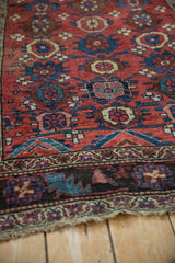 Low angle showing the coarse, hand-knotted texture and dark floral border of an antique Kurdish rug.
