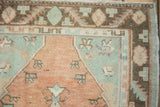 Distressed Oushak rug corner, terracotta field, mint green, dark brown serrated border.