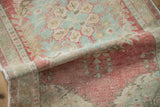 Distressed Oushak rug's rolled edge shows faded raspberry, seafoam green, beige texture.