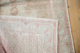 Corner of a distressed Oushak rug folded back to reveal its hand-knotted foundation.