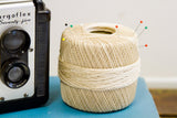 Vintage ecru crochet thread spool with colorful sewing pins stuck in the top.