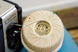 Vintage J&P Coats thread spool used as a pincushion with colorful pins.