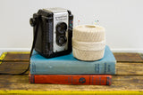 Vintage ecru thread spool styled as a decorative accent with books and a camera.