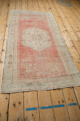 Angled view of a distressed Oushak runner showing its center medallion and blush and seafoam tones.