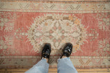 Distressed Oushak runner, worn pile in faded cherry red, ivory, tangerine, and oxidized silver.