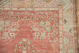 Distressed Oushak rug corner: faded cherry red field and ivory ribboned cloudband motif.
