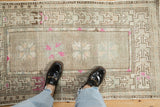 Distressed Oushak rug corner, revealing geometric border and serrated magenta floral motifs.