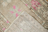 Folded distressed Oushak rug, showing hand-knotted reverse and pink geometric pattern.