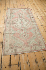 Angled view of a distressed Oushak runner's geometric pattern in faded dusty rose and sea foam green.