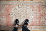 Distressed vintage Oushak runner with faded rose, ivory, and ribboned spandrel motifs beneath feet.