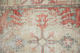 Close-up on the distressed Oushak's weave, showing wear to the cherry red knot heads.